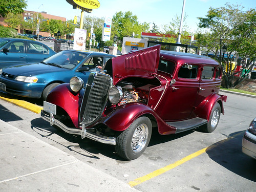 A Burgundycoloured 1934 Ford Model B sedan in the parking lot of a Tim
