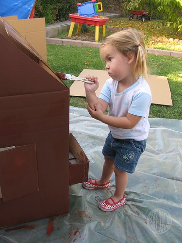 a little girl painting cardboard gingerbread house 
