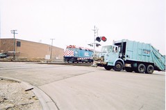A City of Chicago Department of Streets and Sanitation garbage truck, and a westbound Metra commuter train at the North Kilbourn Avenue RR crossing. Chicago Illinois. April 2006.