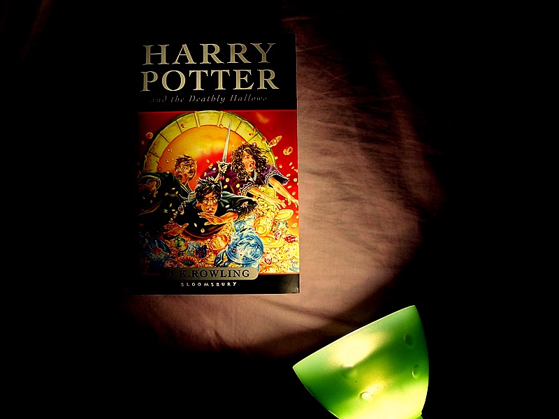 A photograph of the seventh Harry Potter book shrouded in darkness, lit from the bottom right corner by a green lamp.