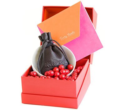 Photo of the Forty Beads gift set: an open red box with forty red beads, a white bowl and a leather drawstring pouch inside.