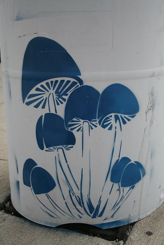 stencil graffiti of a bunch of mushrooms growing out of the concrete, painted at the base of a  post