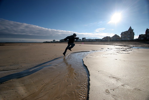 Un enfant saute au dessus d'un ruisseau, sur une plage