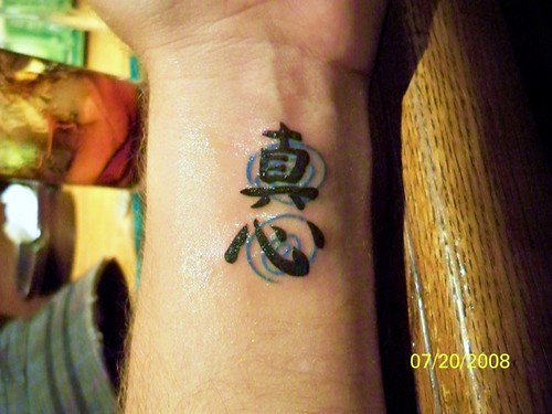 The tattoo says 'magokoro' in kanji, with light blue swirls behind it.