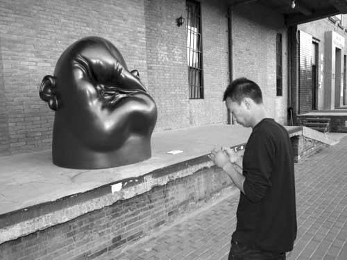 A visitor to the 798 art district looks at his photos, while a crushed face looks at him.