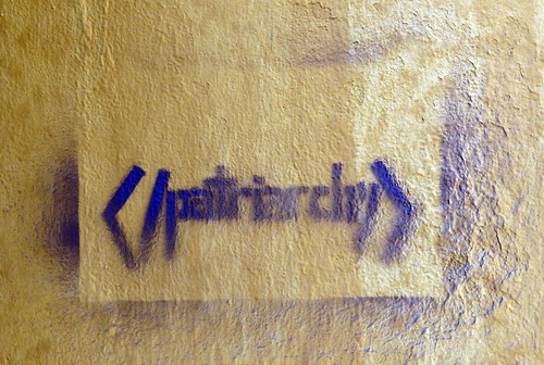 A graffiti in purple ink on a black wall, exhorting people to end patriarchy.