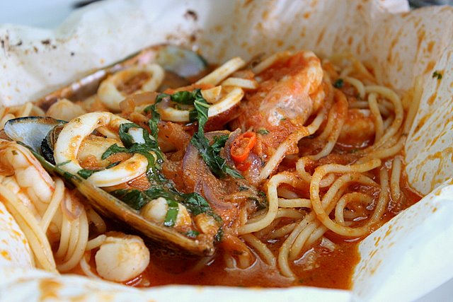 Pasta Cartoccio - spaghetti with sauteed squid, prawns, clams and mussels in light tomato sauce, garlic and white wine, bagged in foil