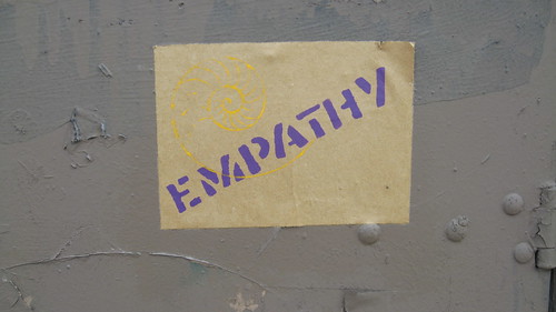 a wheat-pasted poster with the word EMPATHY in purple bold lettering. A yellow outline of a nautalus shell is just over the beginning of the word.