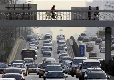 A man rides his bicycle across a pedestrian bridge as cars travel on the road below