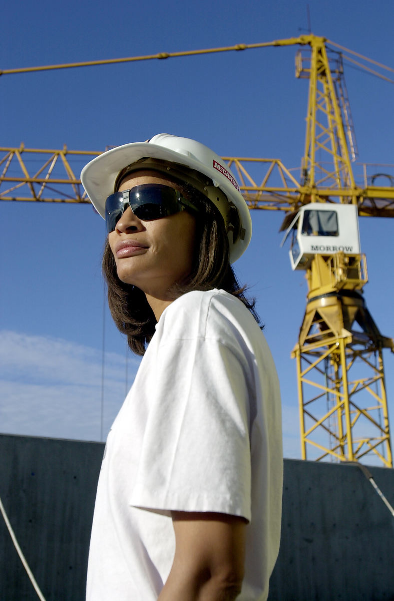 woman at construction site wearing a white tshirt, sunglasses, and hard hat