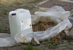plastic bottle containing unknown substance with warning label: assorted rubbish nearby (flickr)