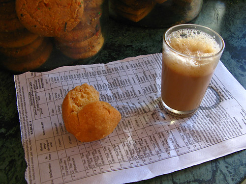 Frothy chai and coconut fritter served on a piece of newspaper at a stand