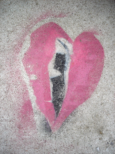 graffiti on concrete: red-pink heart with a black streak down the center --