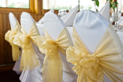 Chairs Covered in White and Decorated with Gold Bows for a Wedding Reception