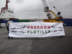 [Devant un navire freegaza.org accosté, deux personnes tiennent une banderole Freedom Flotilla]