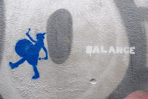 graffiti: to the far right, the word Balance, then a grey circle, the, to the far right, a blue bass drummer, marching away