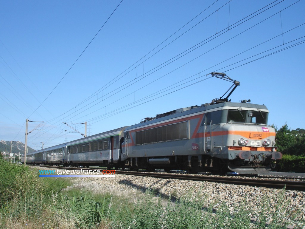 Une locomotive bi-tension BB 22200 SNCF en livrée béton tracte un train voyageurs sur la ligne Marseille - Nice.
