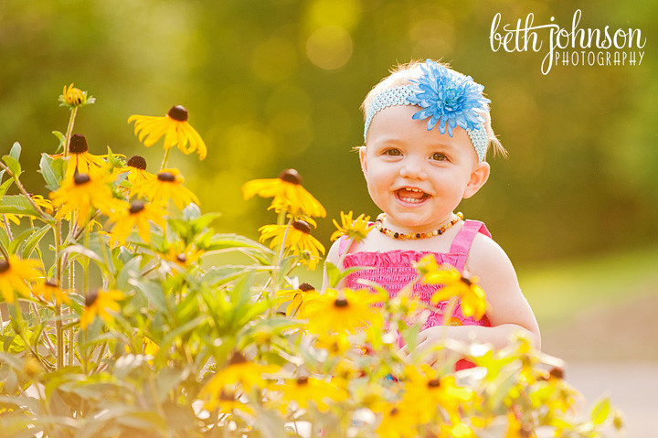 one year old girl in front of yellow flowers
