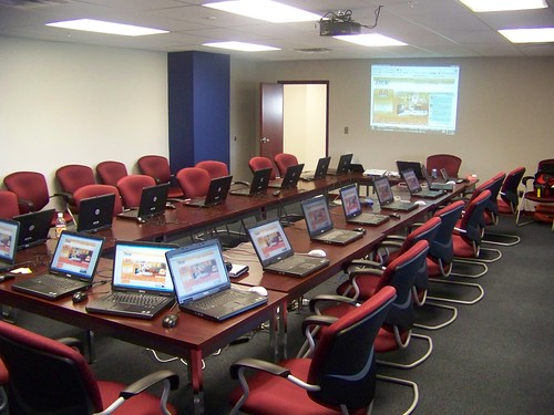 a square table surrounded by lots of chairs and laptops in a conference room.
