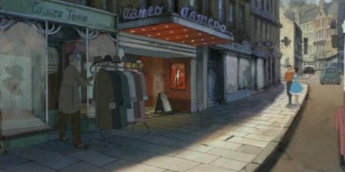 The illusionist spies on Alice and her new boyfriend from behind a coat rack as they're walking down the street. It's sunny, and the characters are in front of a movie theatre called "Cameo". Alice is wearing a blue dress with white trim at the bottom, her boyfriend is wearing an orange shirt with dark pants, and the magician's clothes are dark.