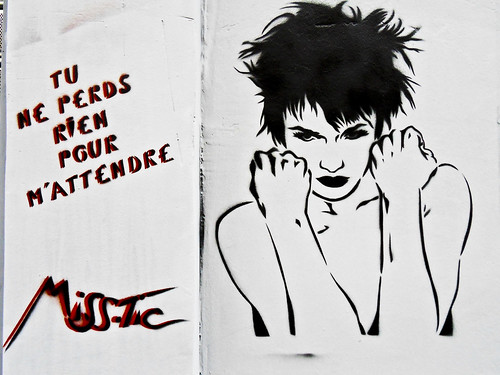 graffiti of a short haired woman raising her fists, next to the words 'Tu ne perds rien pour m'attendre'