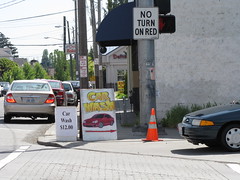 Two sidewalk signs in the right-of-way at 15th and Beacon. The car on the right is about to enter the intersection (and crosswalk) and make an illegal right turn onto 15th (the light was red by the time they made the turn, and the intersection is No Right on Red.) Photo by Wendi.