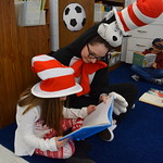 Student in Cat in the Hat costume helps elementary student read a book