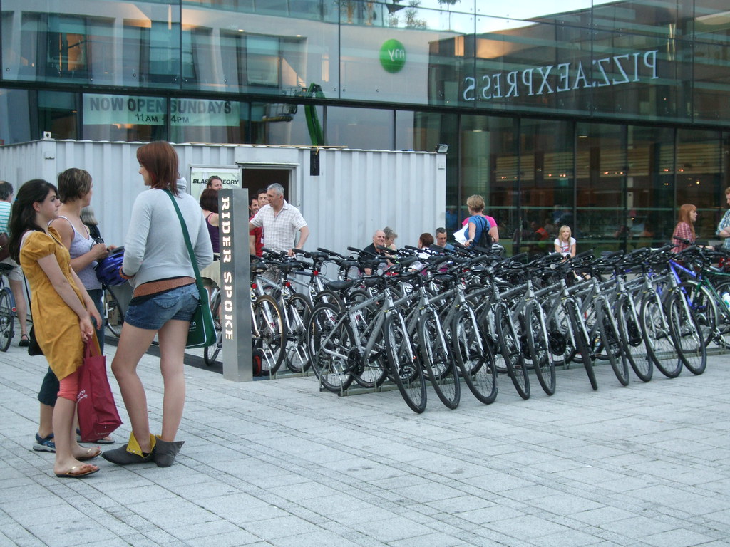 Bicycles are lined up in racks with illuminated signage and shipping container for induction briefings.