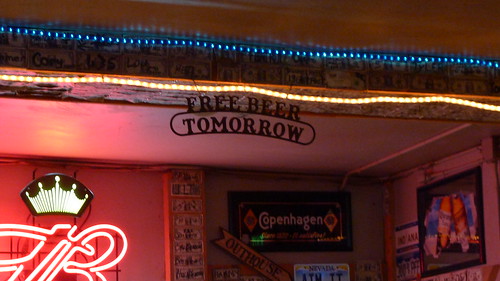 Upward view of a sign reading, Free Beer Tomorrow, with string lights over it, inside of a bar