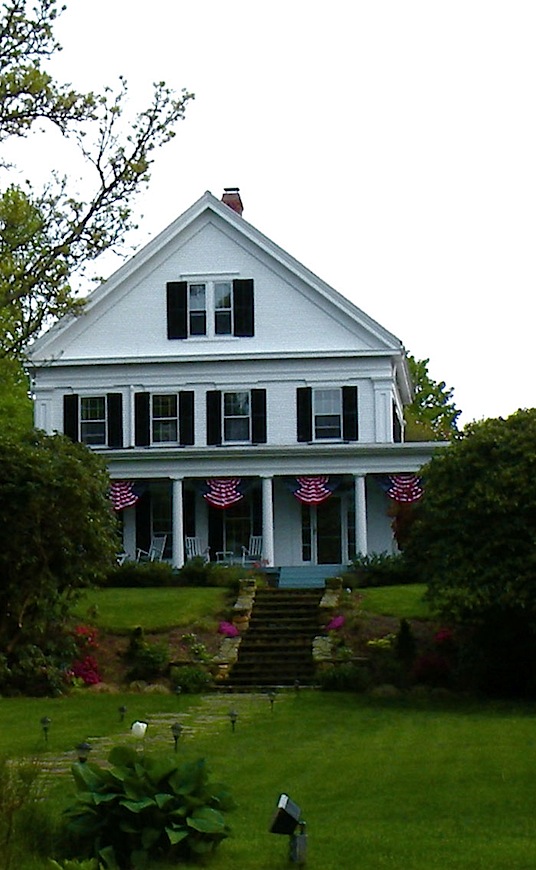 A white Greek Revival house with deep porch and patriotic bunting on Cape Cod. 
