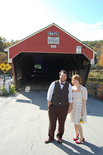 bride and groom in front of covered bridge