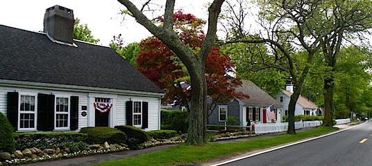 Three small white Cape Cod style homes in Barnstable MA with red, white and blue bunting for the 4th of July. 